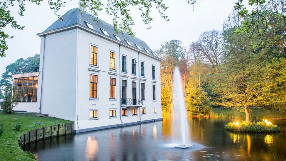 Landhuis Te Werve bij schemer, met verlichte ramen en fontein in de vijver